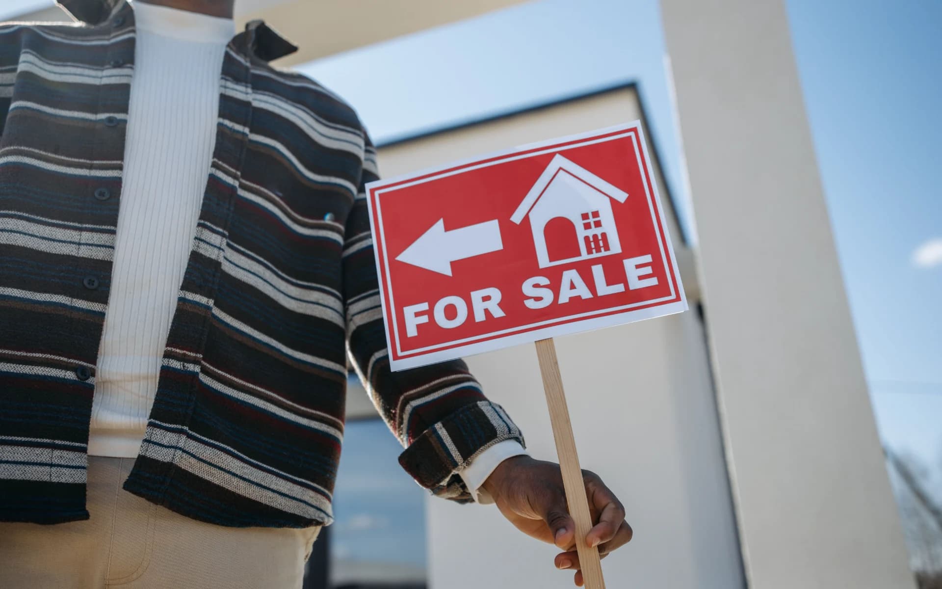 A person holding a red For Sale sign outside a house that has just come on the market