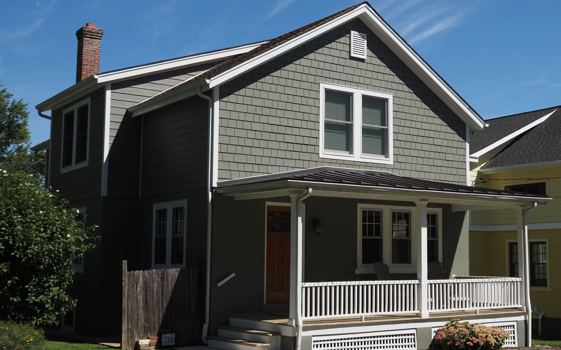 A two-storey clapboard house with a covered front porch, seen from the street on a clear day