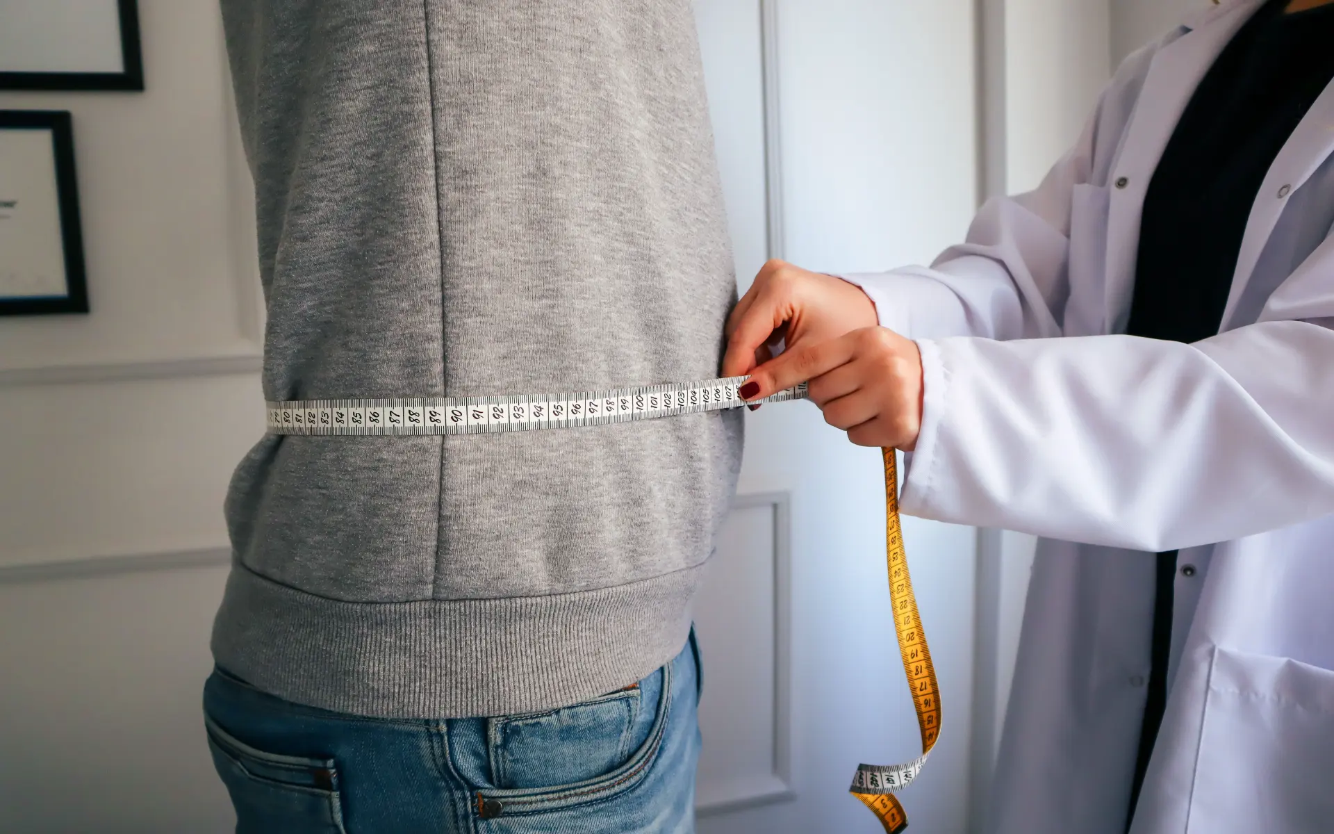 A clinician measures a patient's waist with a tape measure, the reading just past 100 centimetres