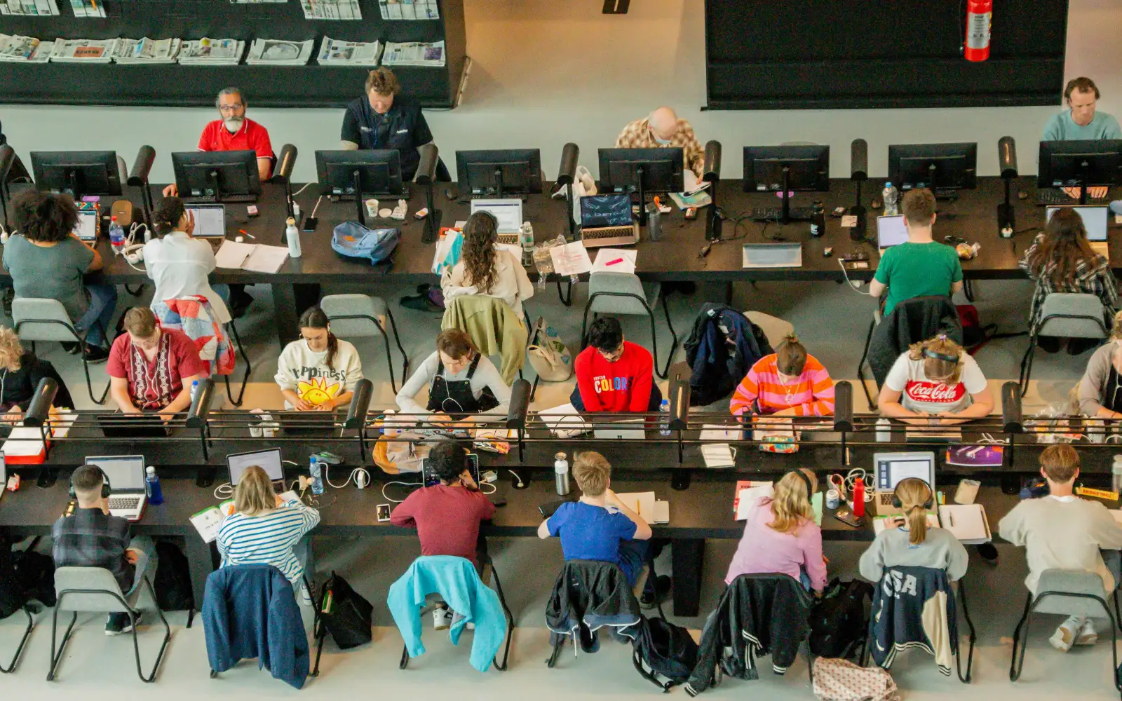 A university study hall seen from the floor above, every desk along the rows taken by a student working through coursework