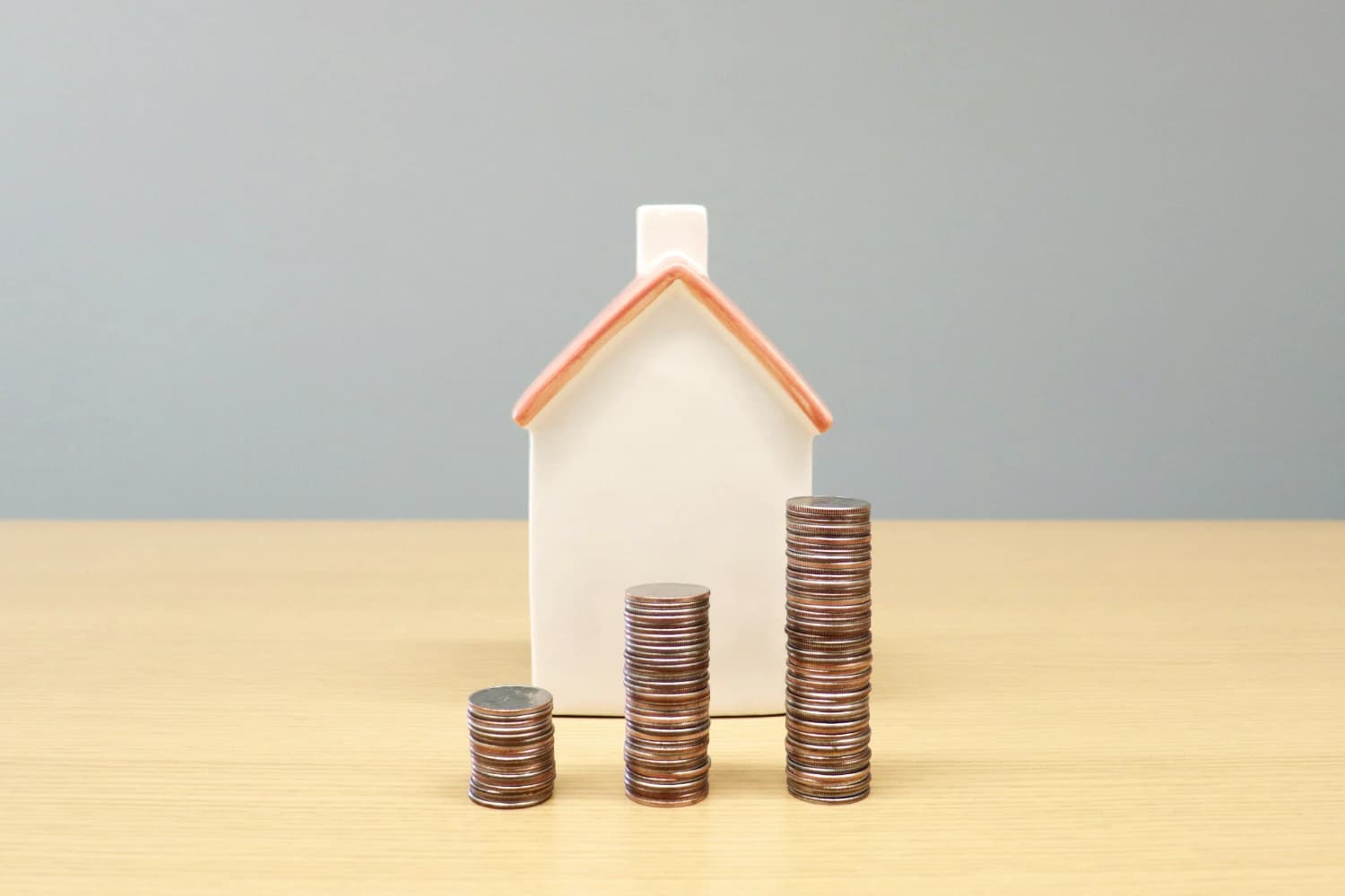 Three stacks of coins rising in front of a model house as a deposit is saved up